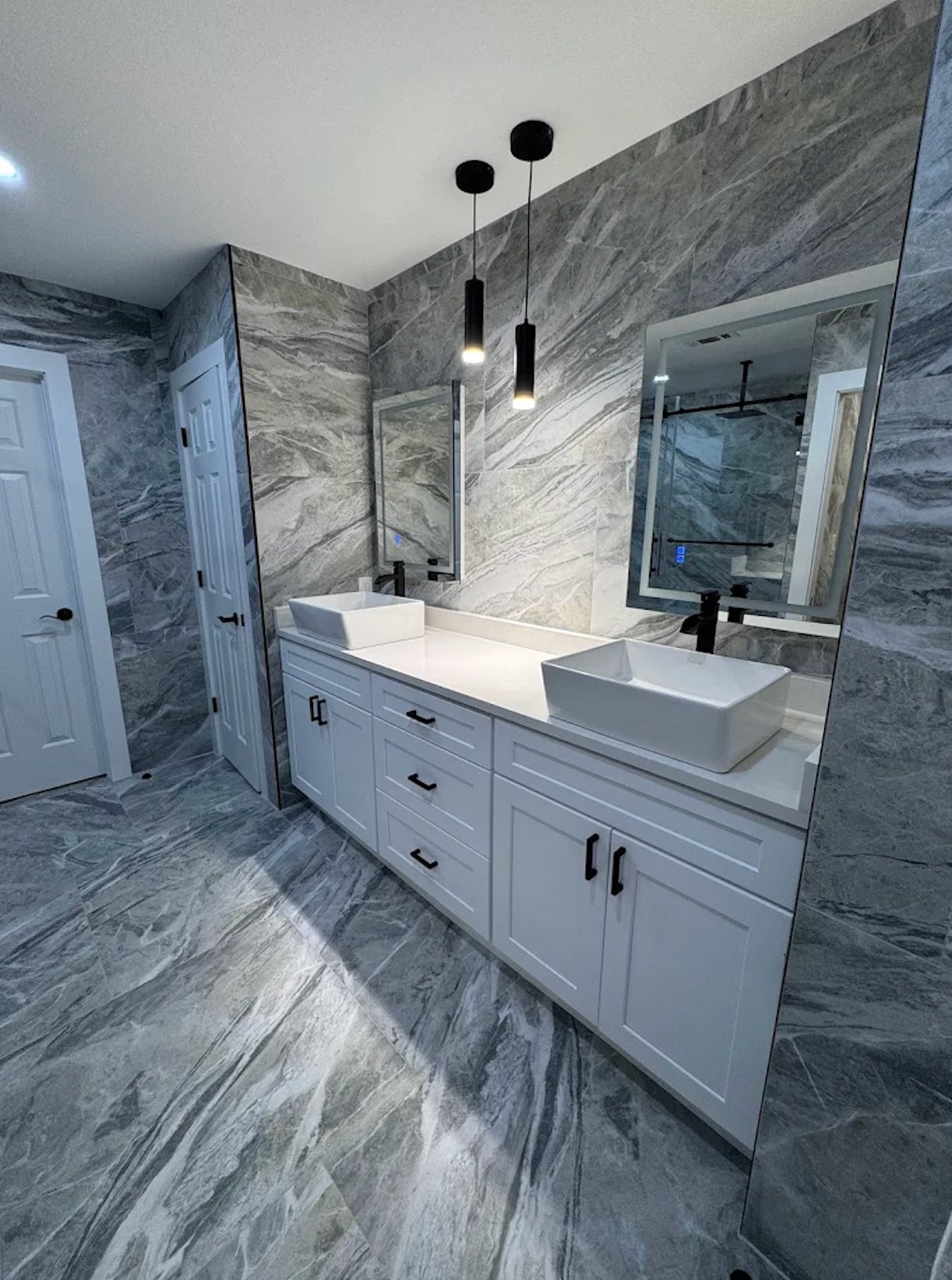 Bathroom remodel with floor-to-ceiling marble tile, dual vessel sinks, pendant lights, and white shaker vanity by Alphex Painting and Remodeling