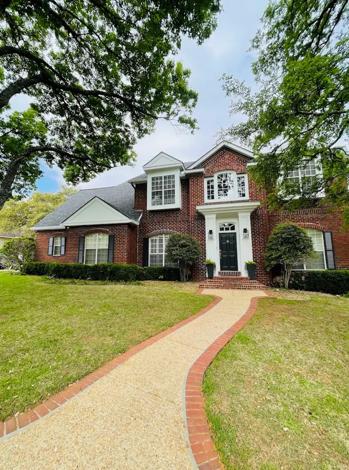 Beautiful two-story brick home exterior with freshly painted trim, shutters, and front door by Alphex Painting and Remodeling