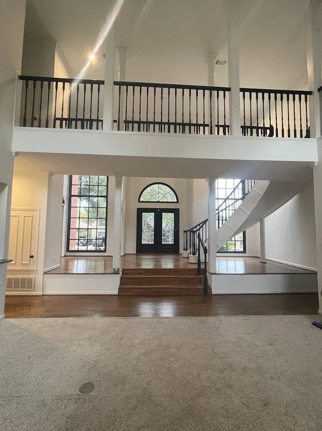 Two-story foyer with freshly painted white walls, black iron railing, hardwood entry, and grand staircase by Alphex Painting and Remodeling