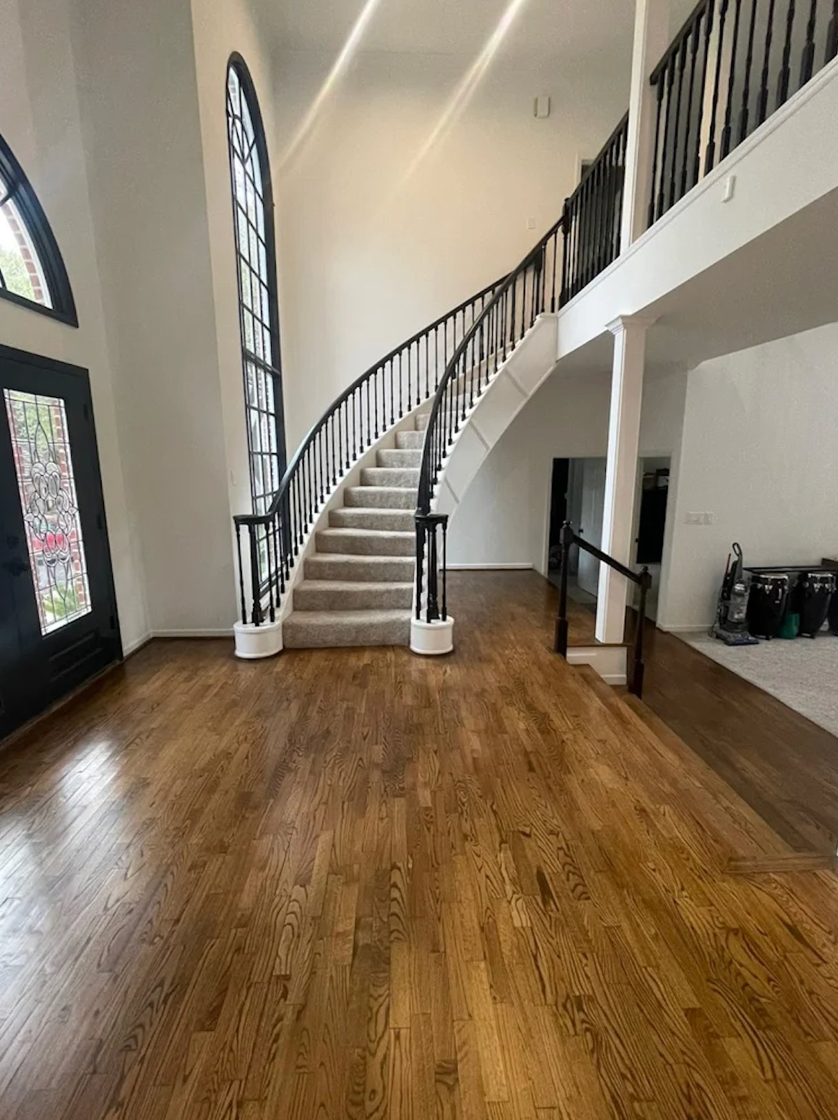 Grand curved staircase with painted black iron balusters, stained glass window, and refinished hardwood flooring by Alphex Painting and Remodeling